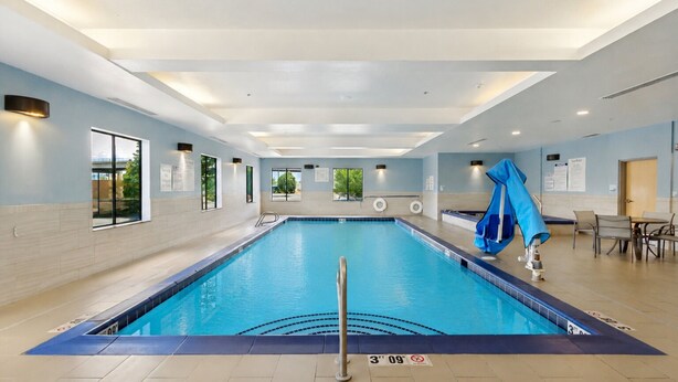 Una piscina interior con agua cristalina, una silla de salvavidas y una mesa con sillas junto a la piscina.
