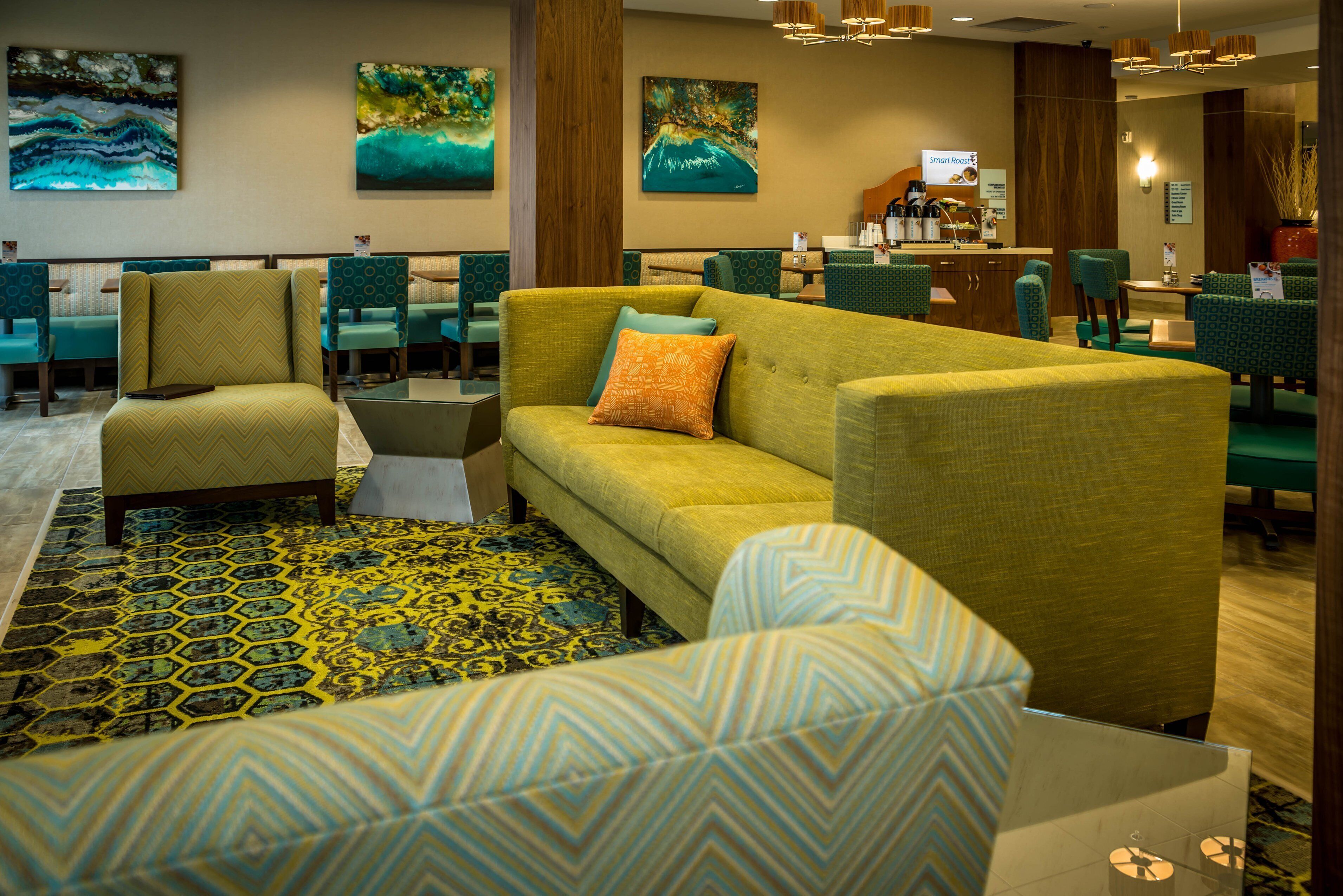 A hotel lobby with a green sofa, patterned chairs, and artwork on the walls.