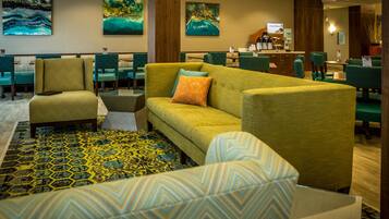 A hotel lobby with a green sofa, patterned chairs, and artwork on the walls.