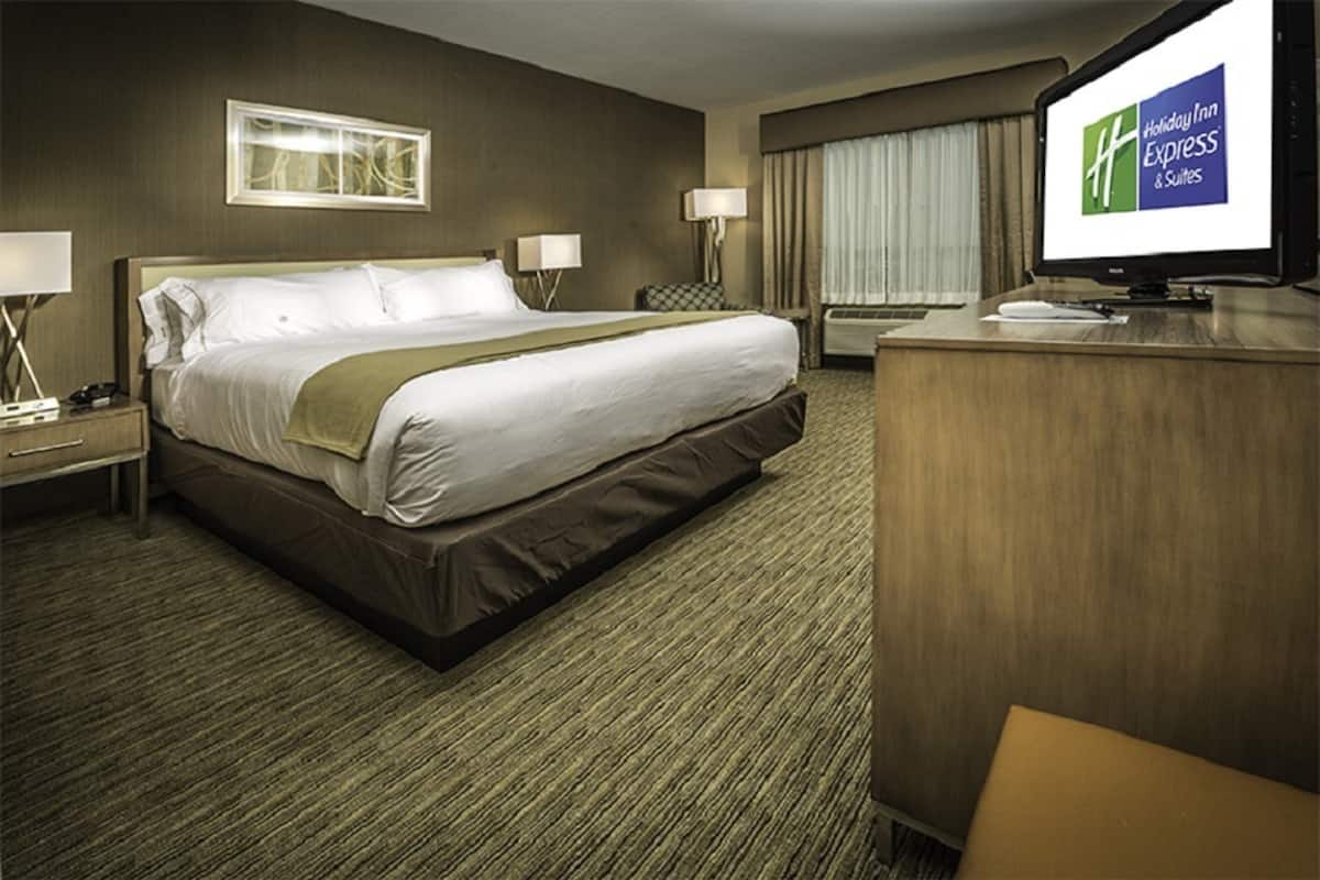 Une chambre d’hôtel avec un grand lit, un bureau, une télévision et une fenêtre avec des rideaux.