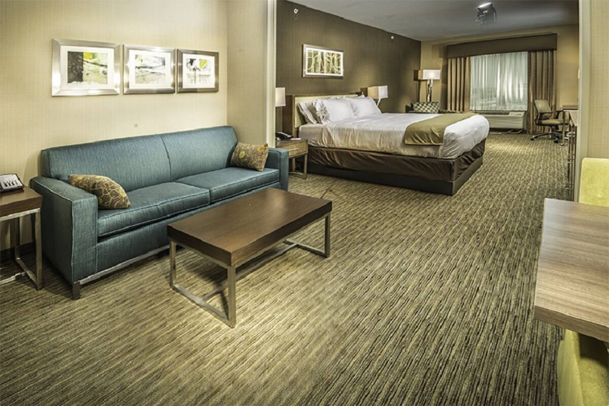 A hotel room with a bed, a sofa, a coffee table, and framed pictures on the wall.