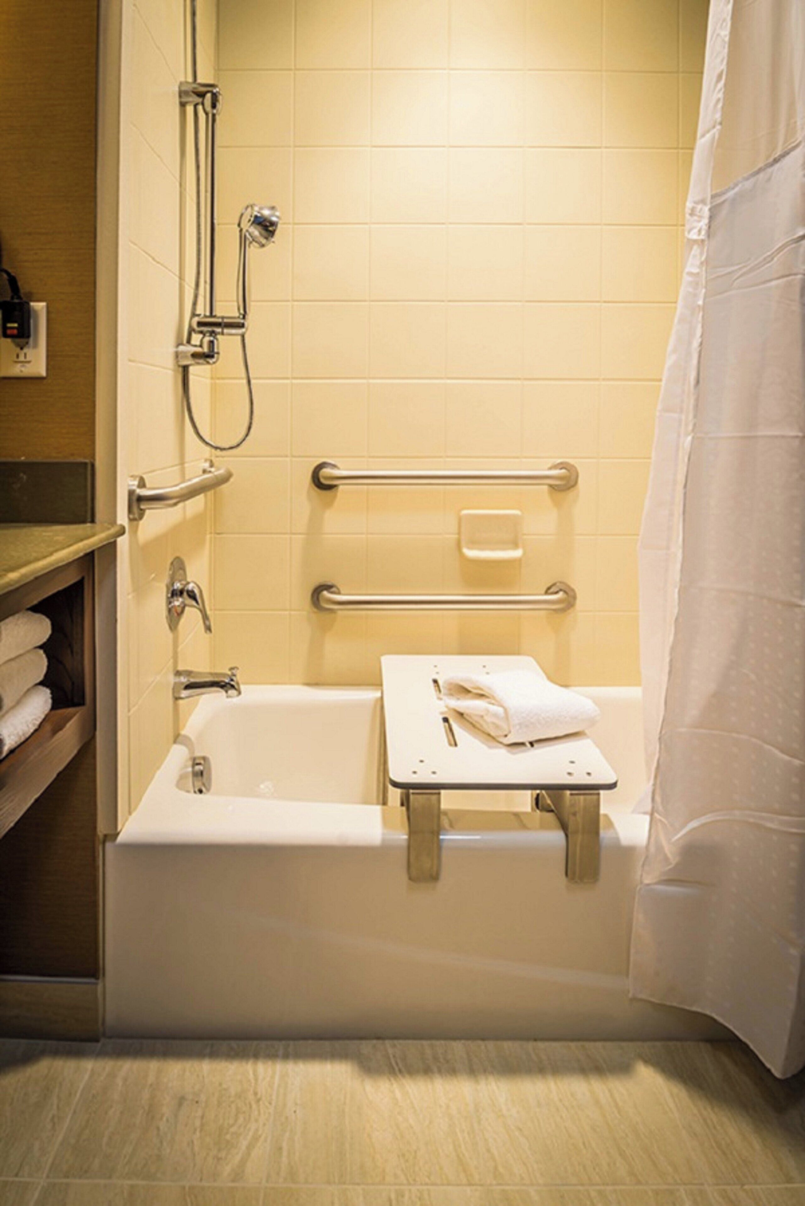 A bathroom with a bathtub, a shower, and a handrail for accessibility.
