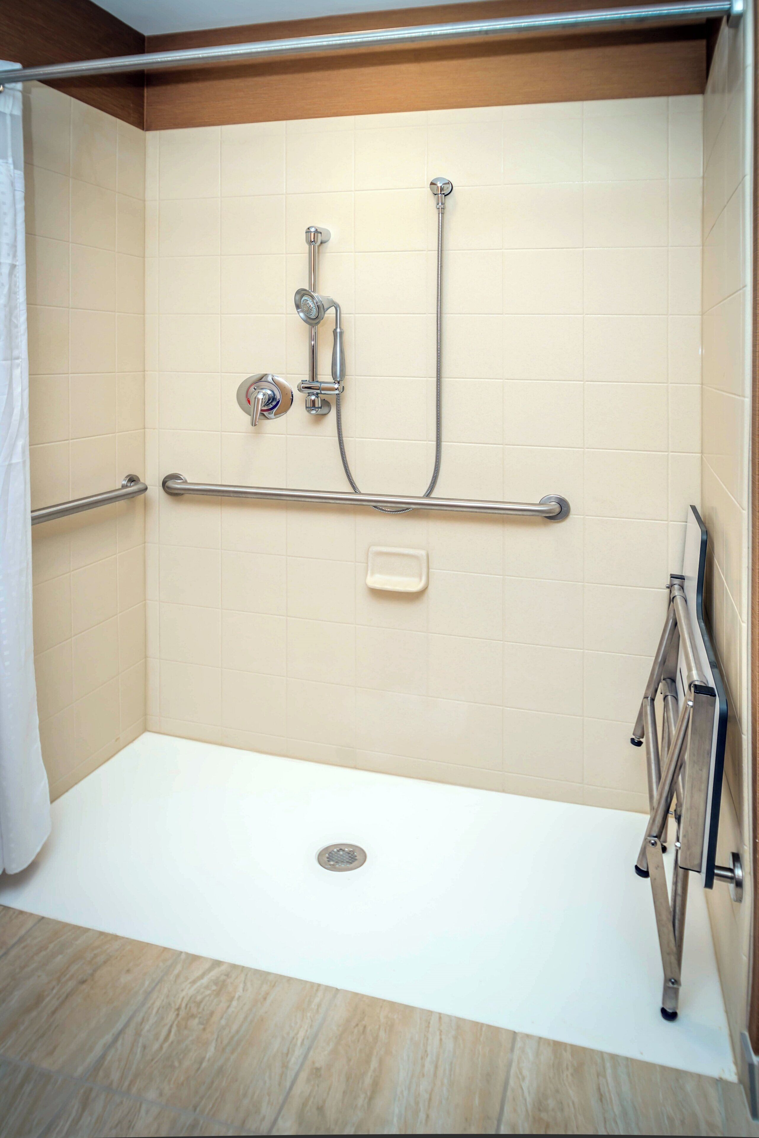 A shower area with a grab bar, a handheld showerhead, and a handheld faucet.