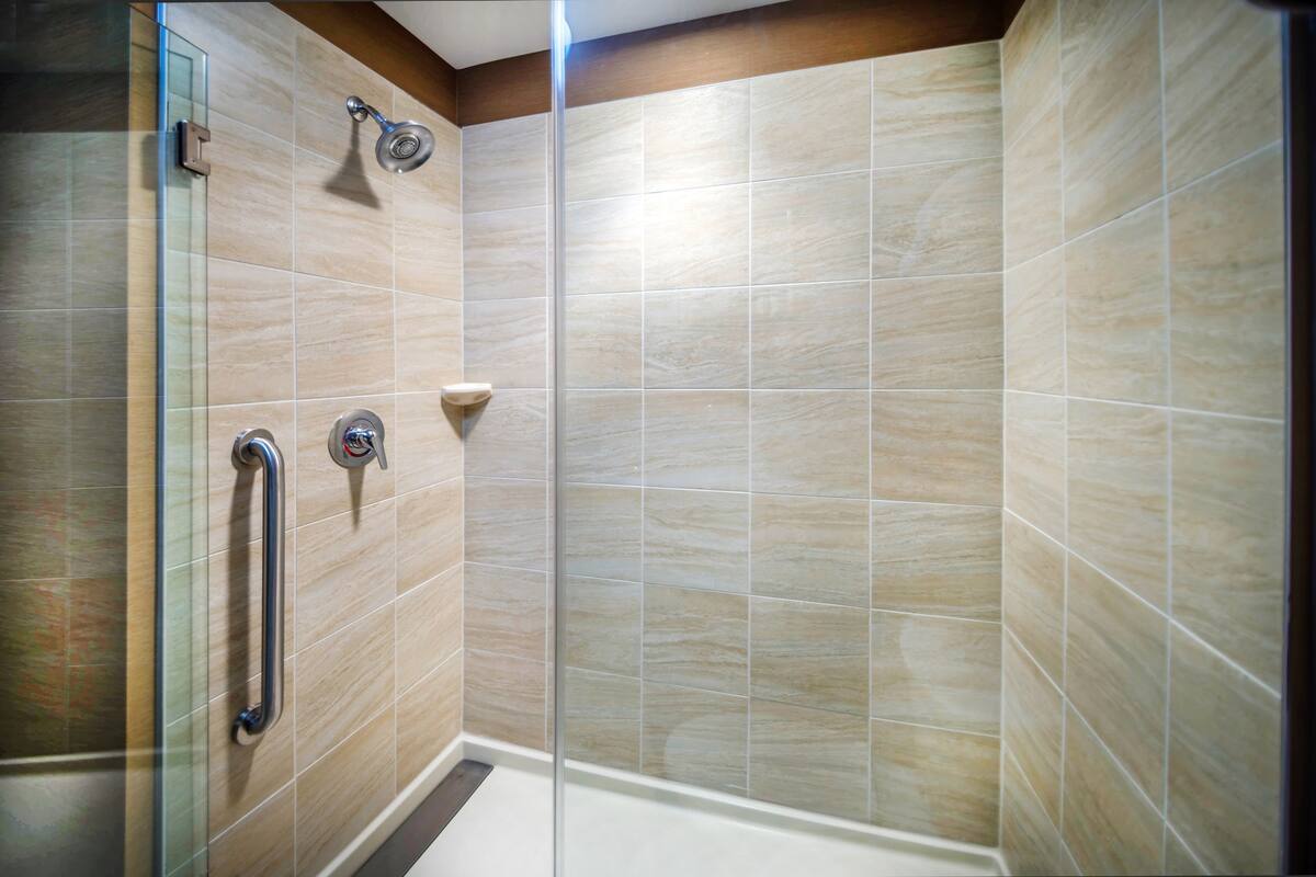 A shower with a glass door, a handrail, and a wall-mounted showerhead.
