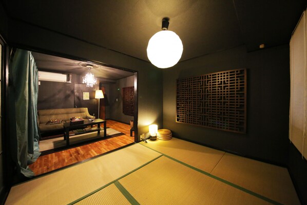 Una habitación japonesa tradicional con suelo de tatami, una mesa baja, un sofá y una lámpara colgante.