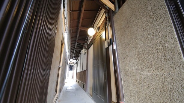 A narrow corridor with a metal door on the right and a wooden door on the left.