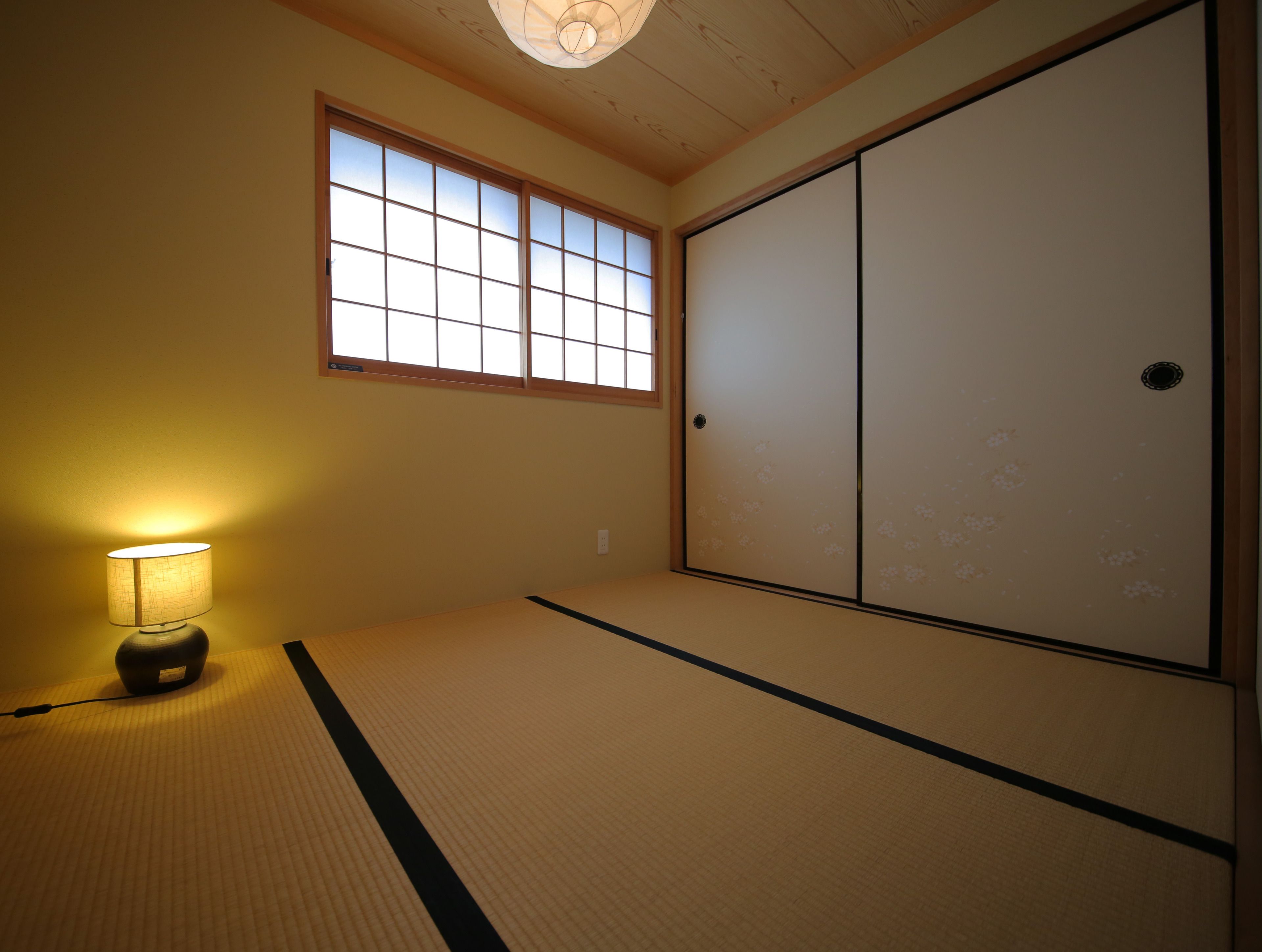 A traditional Japanese room with tatami flooring, a sliding shoji door, and a lamp.