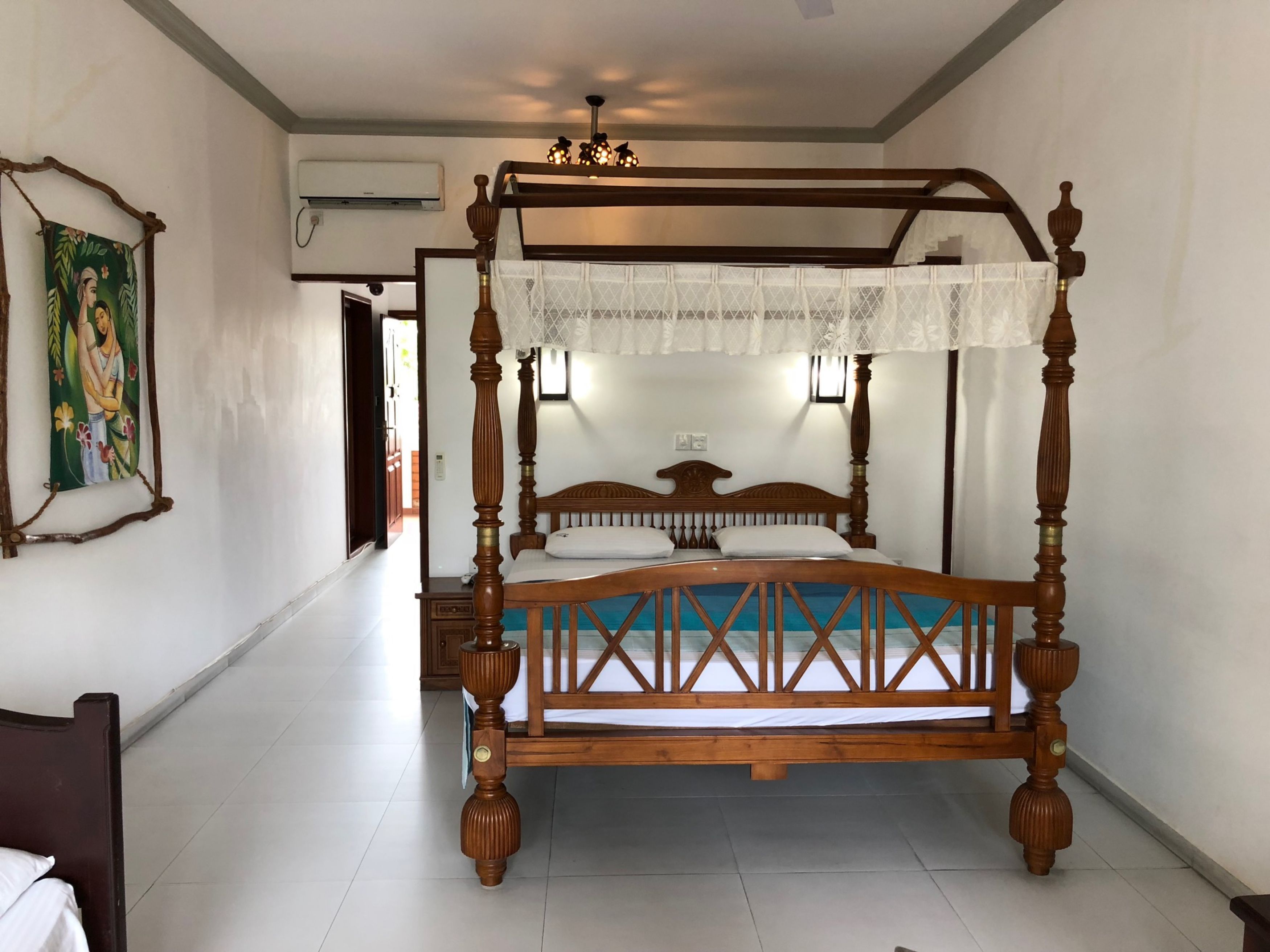 A four-poster bed with a wooden frame and a canopy, a painting on the wall, and a ceiling fan.