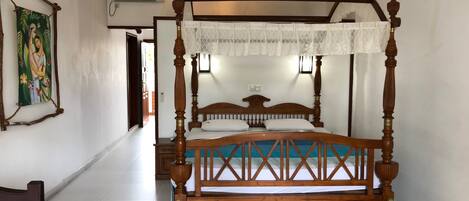 A four-poster bed with a wooden frame and a canopy, a painting on the wall, and a ceiling fan.