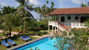 A pool area with lounge chairs and a building with a tiled roof. - Wunderbar Beach Hotel (Bentota)