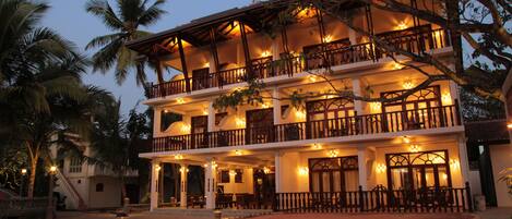 Un hotel de varios pisos con balcones, mobiliario exterior y palmeras.