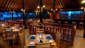 A restaurant with wooden tables and chairs, a bar area, and a view of palm trees. - Wunderbar Beach Hotel (Bentota)