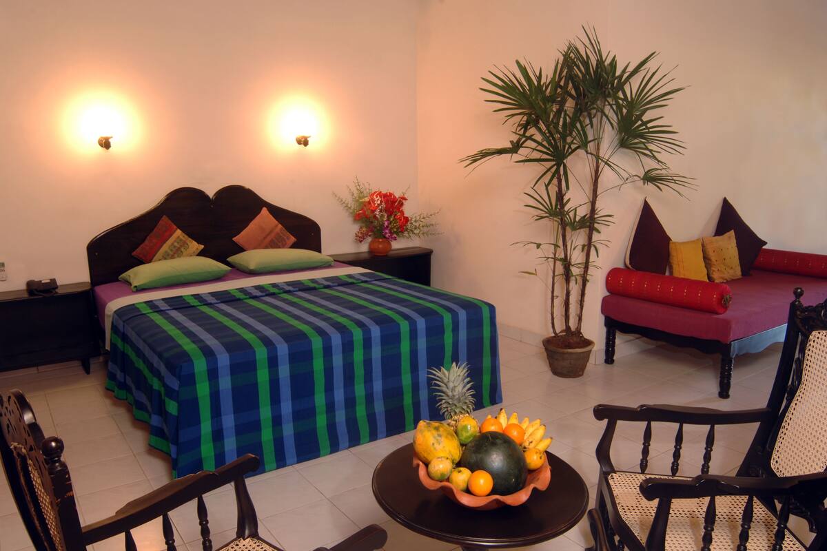 A bedroom with a bed, nightstands, a sofa, a dining table with fruit, and a potted plant.