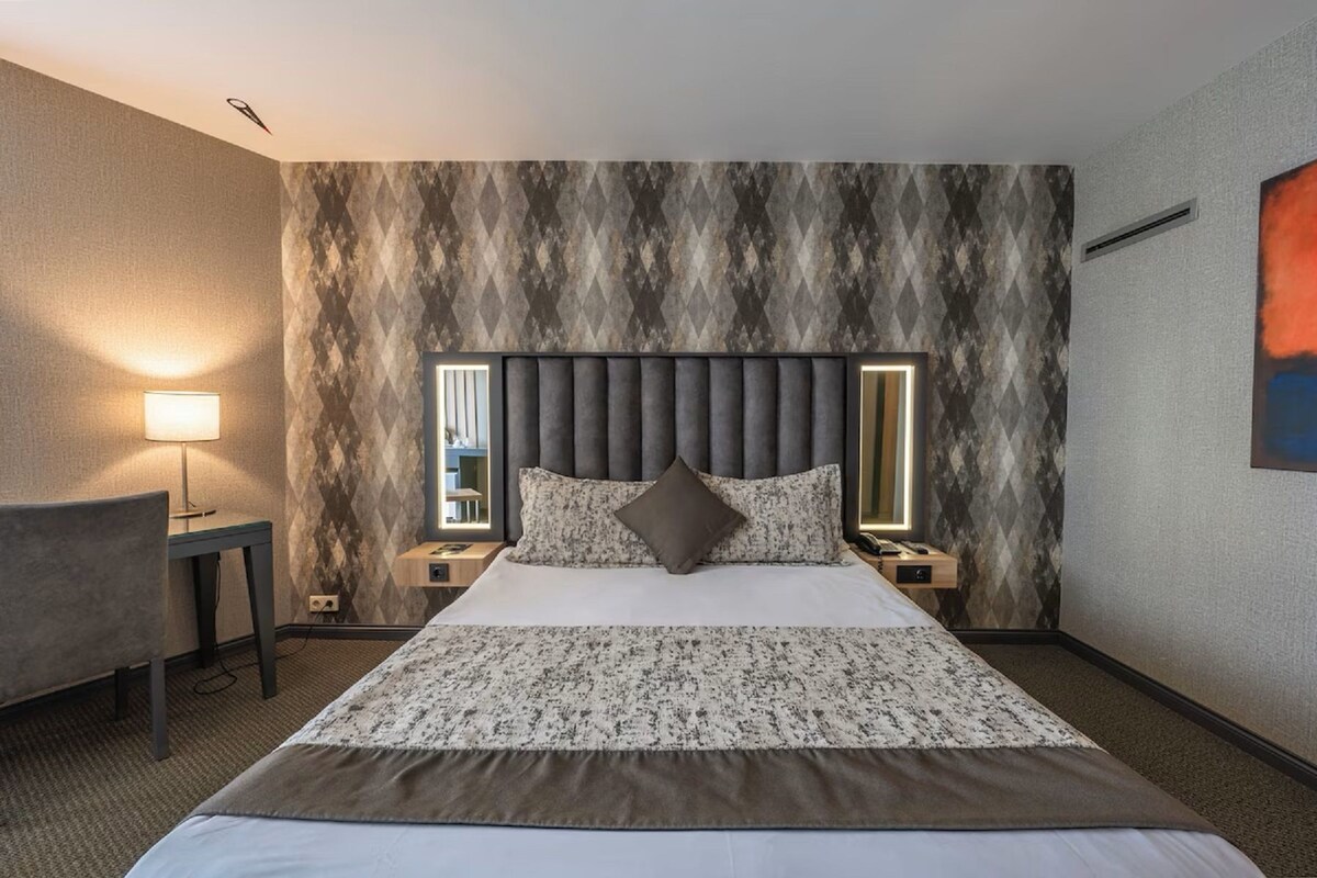 A hotel room with a bed, bedside tables, a lamp, and a wall with a geometric pattern.