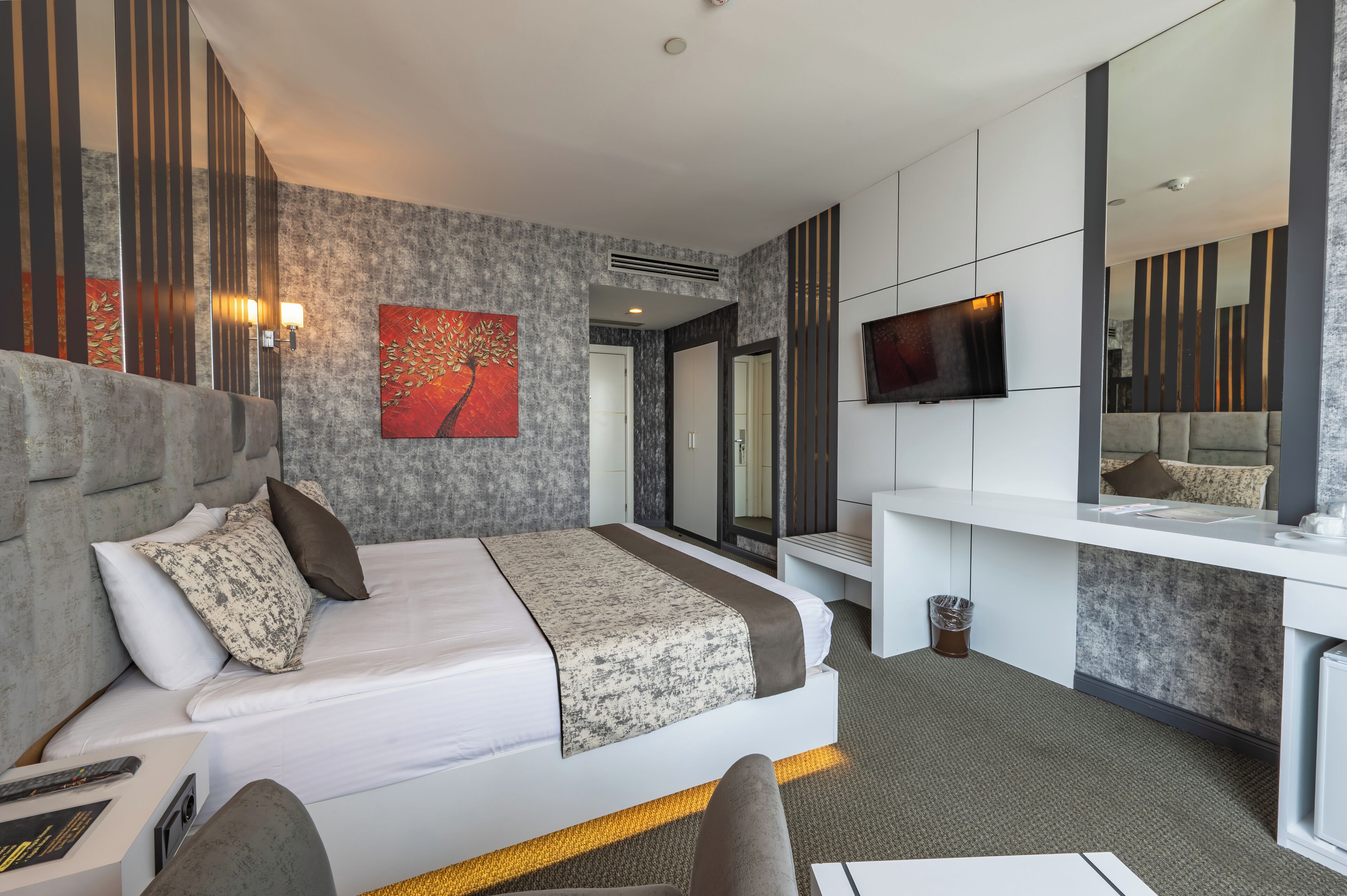 A modern hotel room with a large bed, a desk, a TV, and a mirror.