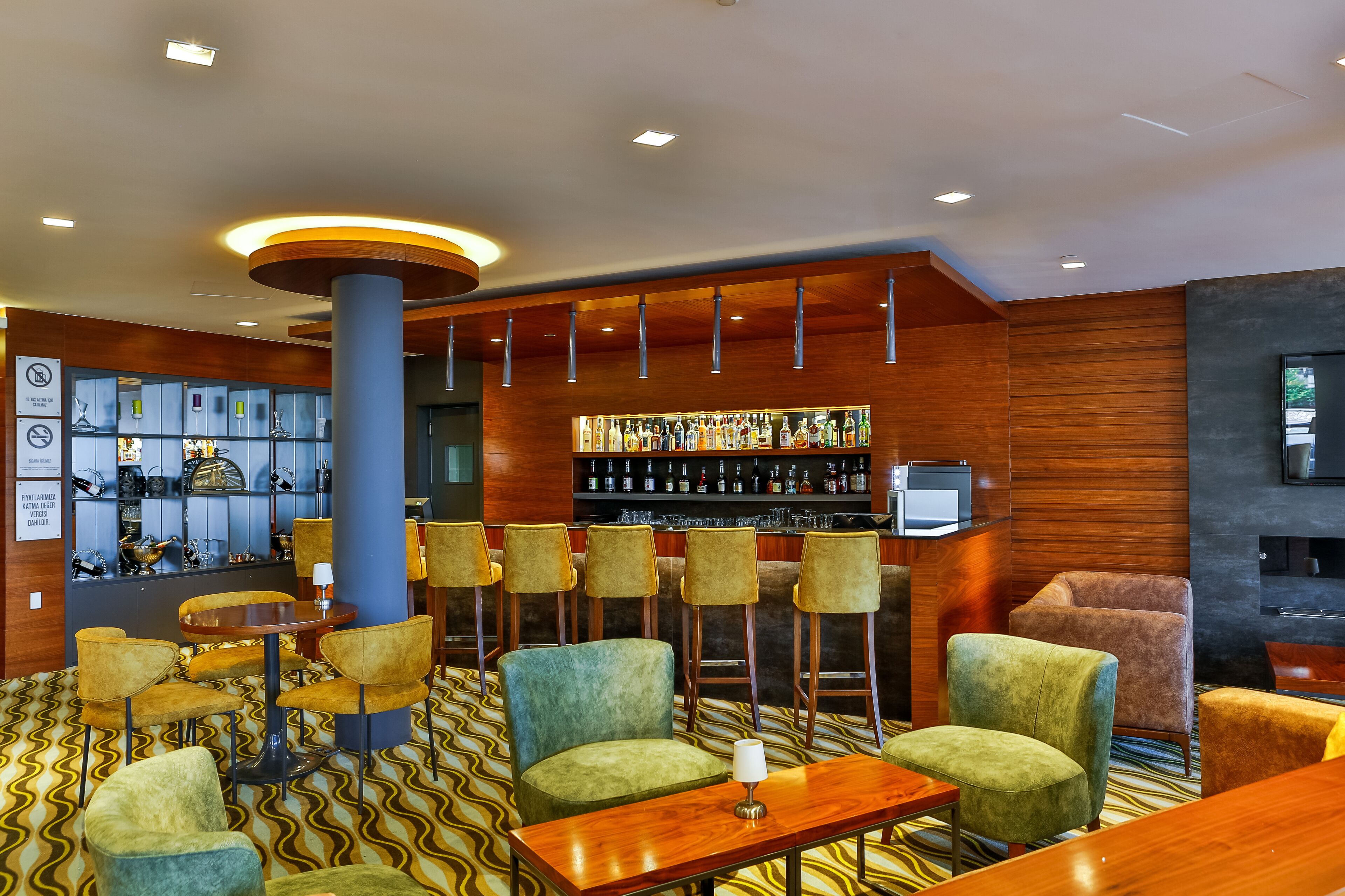 A bar area with multiple seating options, a display of bottles, and a television.