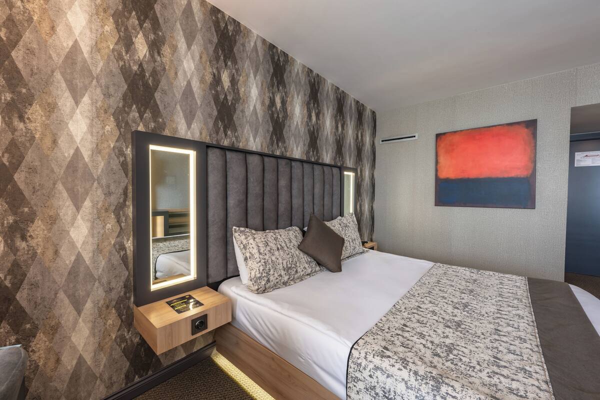 Una habitació d'hotel moderna amb un llit gran, un capçal amb il·luminació integrada, una taula de nit i una obra d'art penjada a la paret.