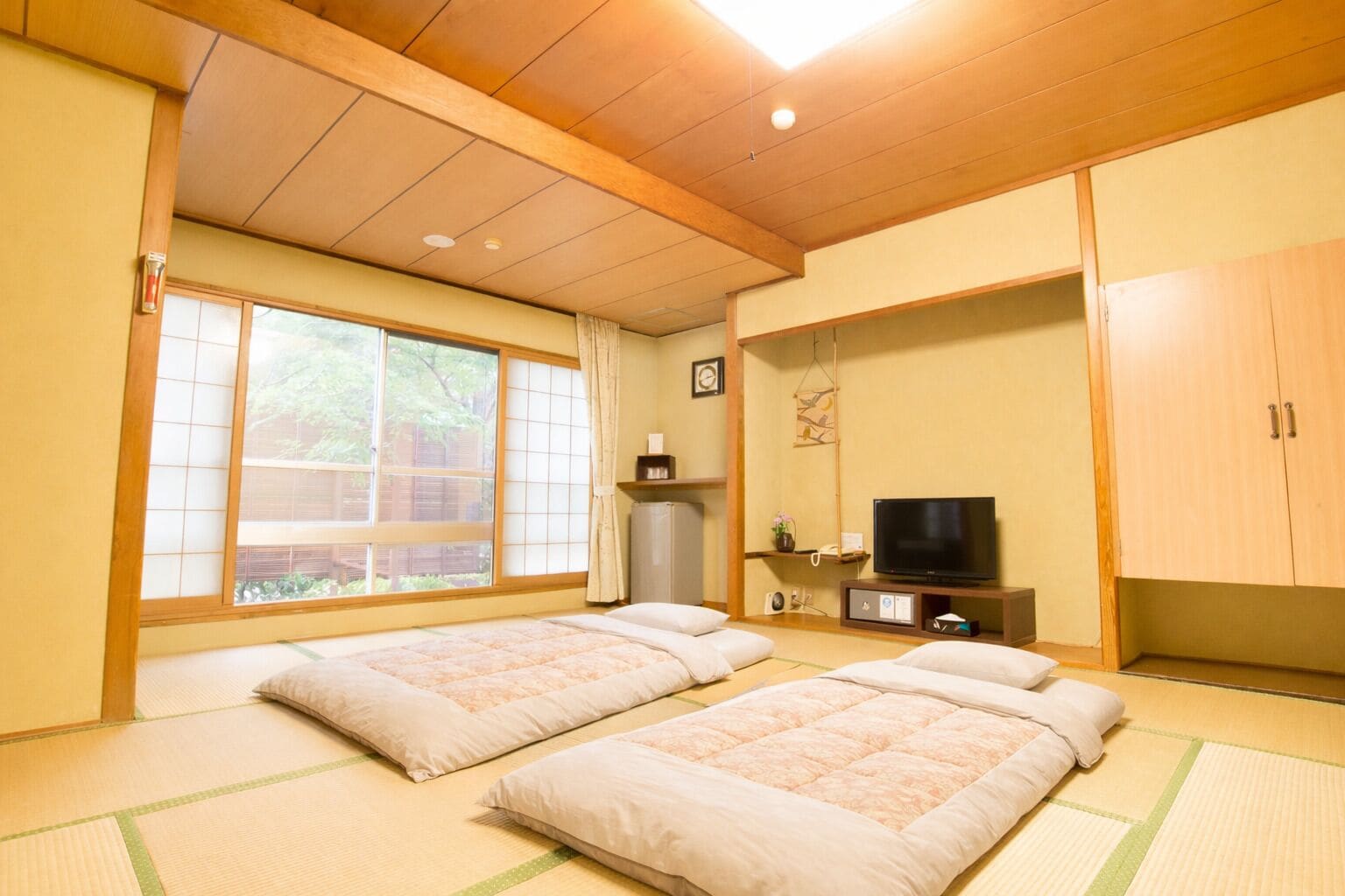A room with tatami mat flooring, two beds, a television, and a cabinet.