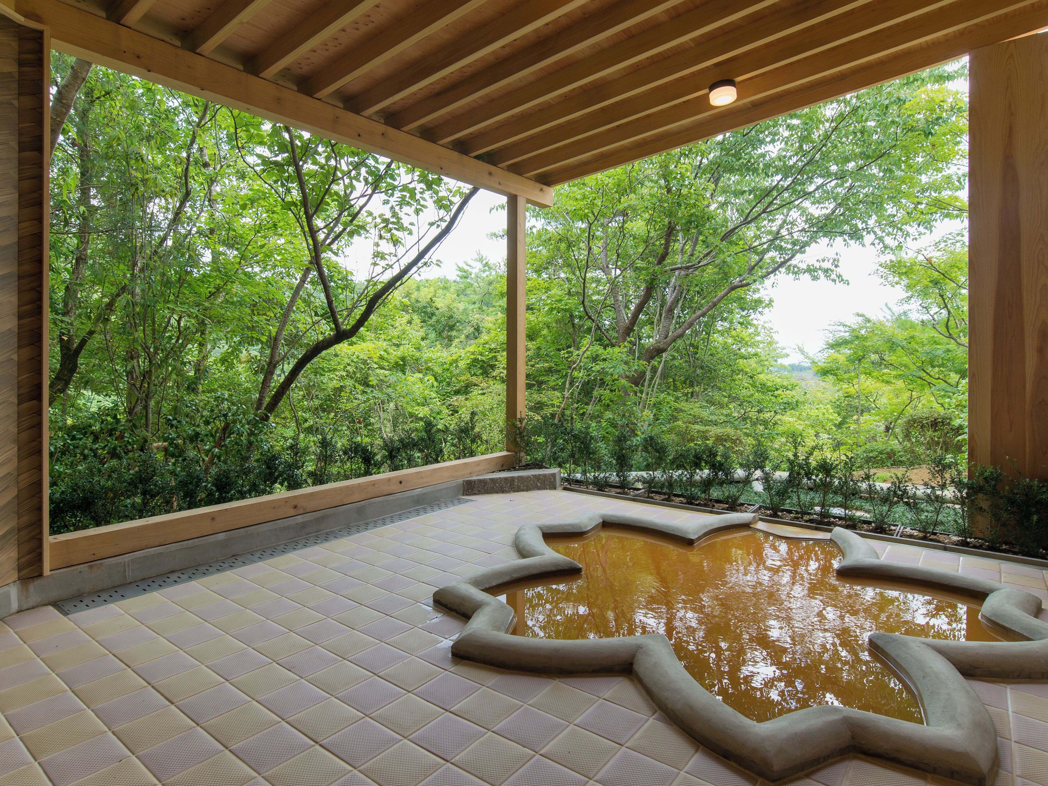 A covered outdoor area with a tiled floor, a central water feature, and a view of lush greenery through large windows.