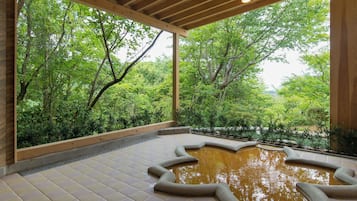 A covered outdoor area with a tiled floor, a central water feature, and a view of lush greenery through large windows.