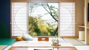 Una habitación japonesa tradicional con suelo de tatami, una mesa baja y un fusuma que ofrece vistas a árboles y montañas.