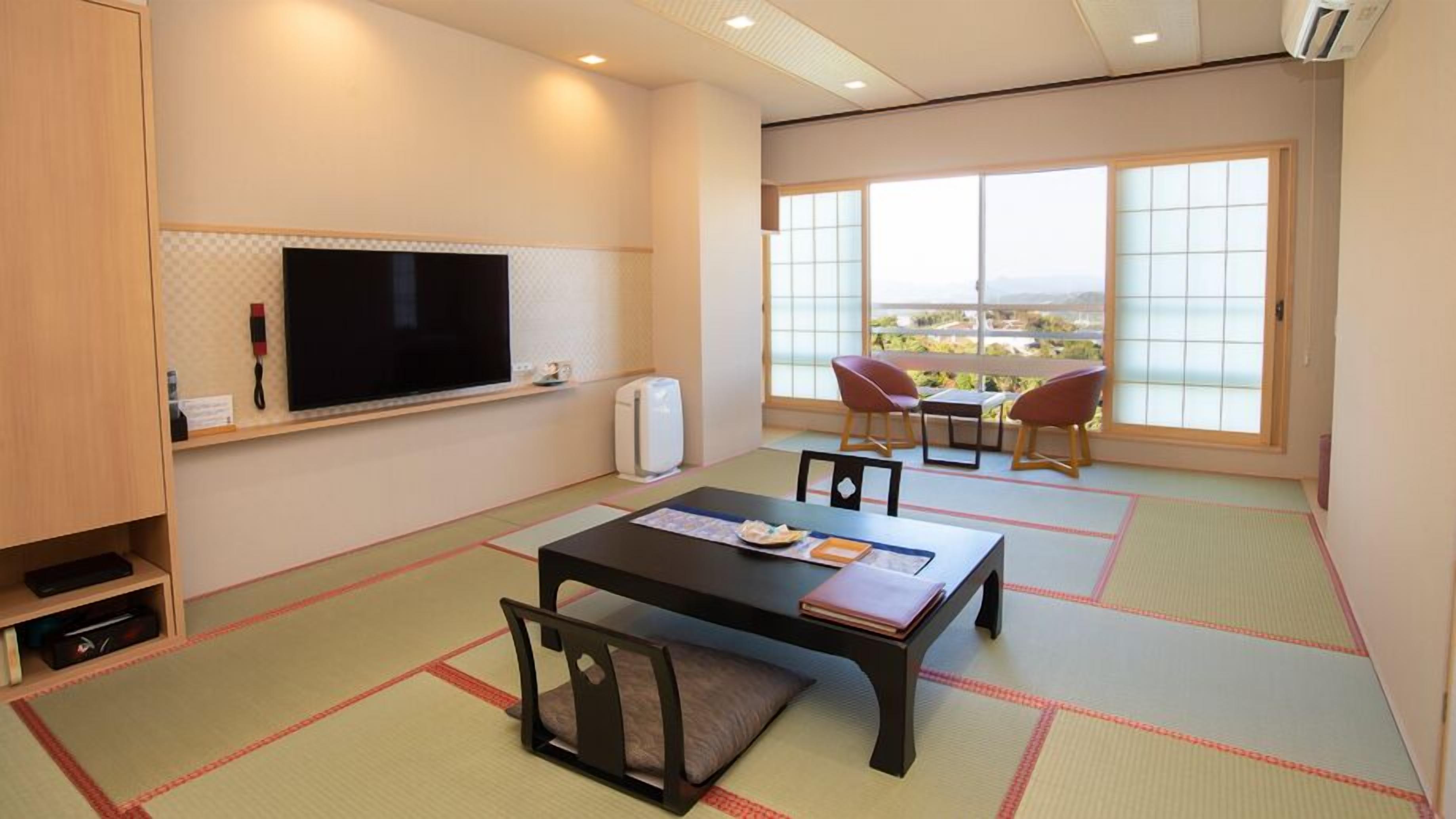 A room with tatami mats, a television, a table with chairs, and a view through large windows.