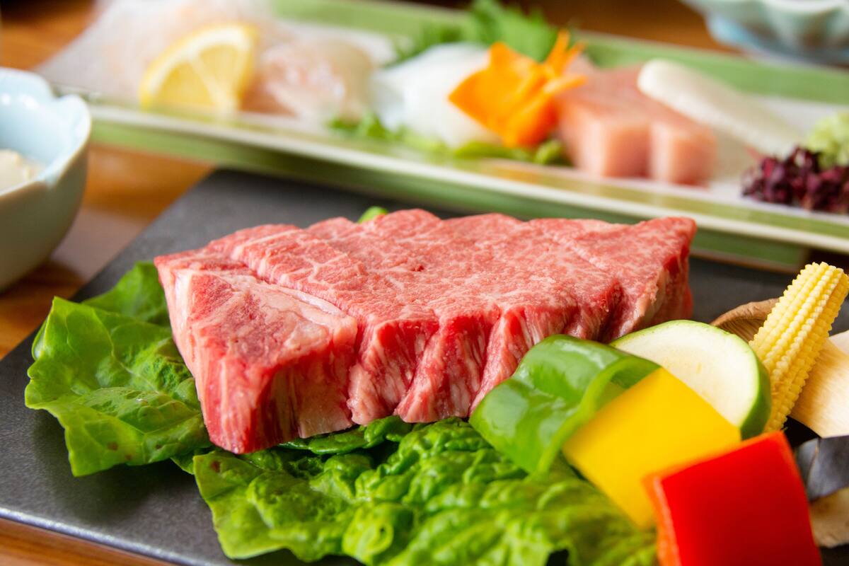 A plate with raw beef, vegetables, and a bowl of soup.