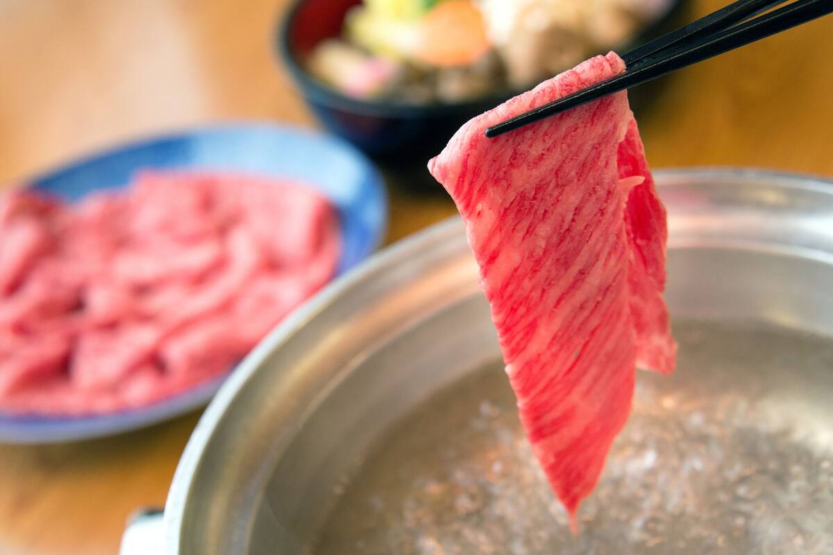 A close-up of a red leaf being held by chopsticks over a bowl of pink food, with a blurred bowl of similar food in the background.