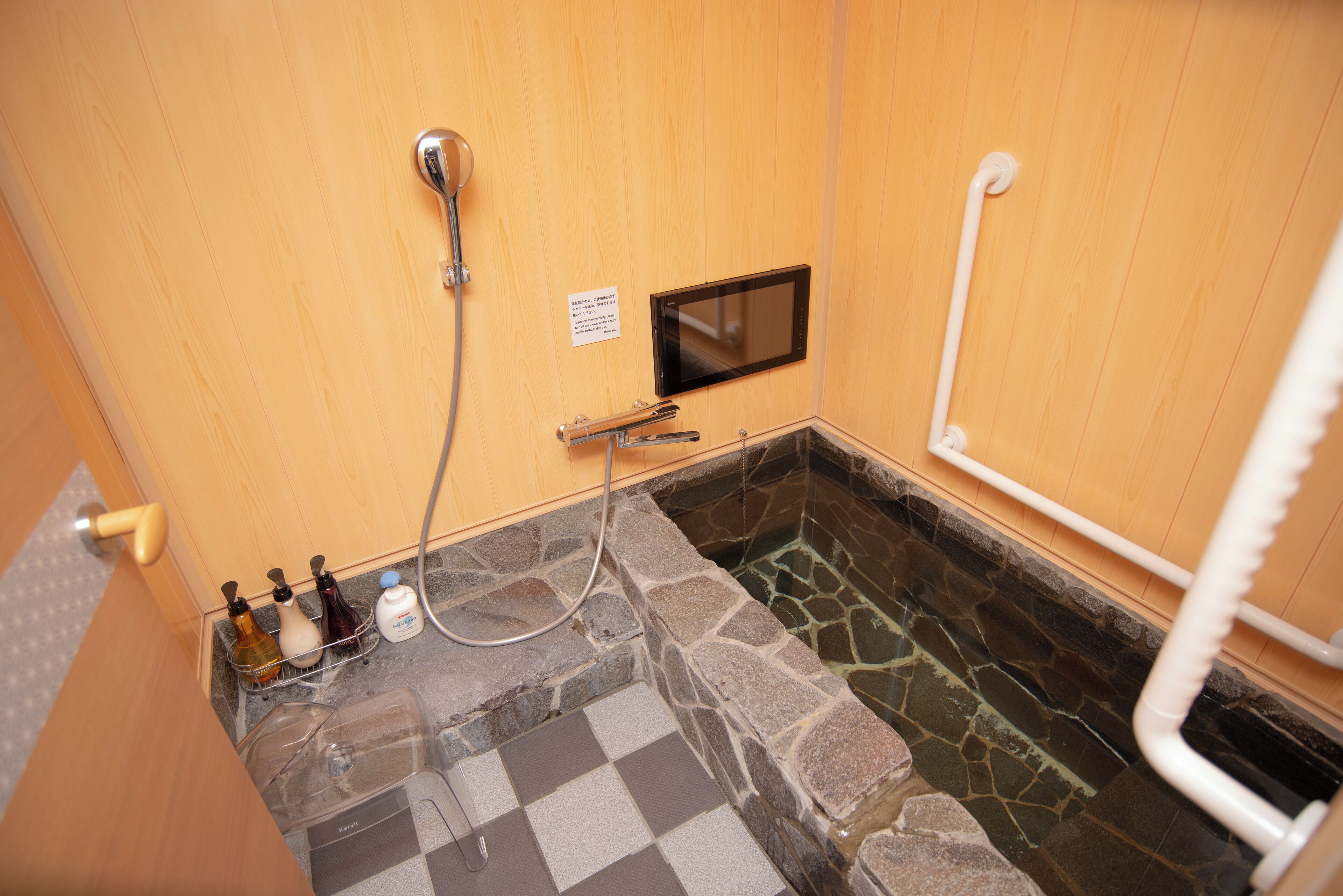 Une salle de bain avec un sol en pierre, un mur en bois, un espace douche et une petite fenêtre.