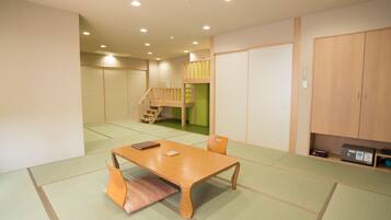 Una habitación japonesa tradicional con suelo de tatami, una mesa de madera baja, un banco acolchado, una puerta corredera verde, una escalera de madera y un armario.