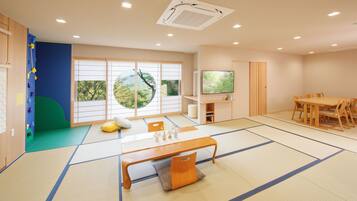 A traditional Japanese-style room with tatami flooring, a tatami mat table, a low wooden table, and a TV mounted on the wall.
