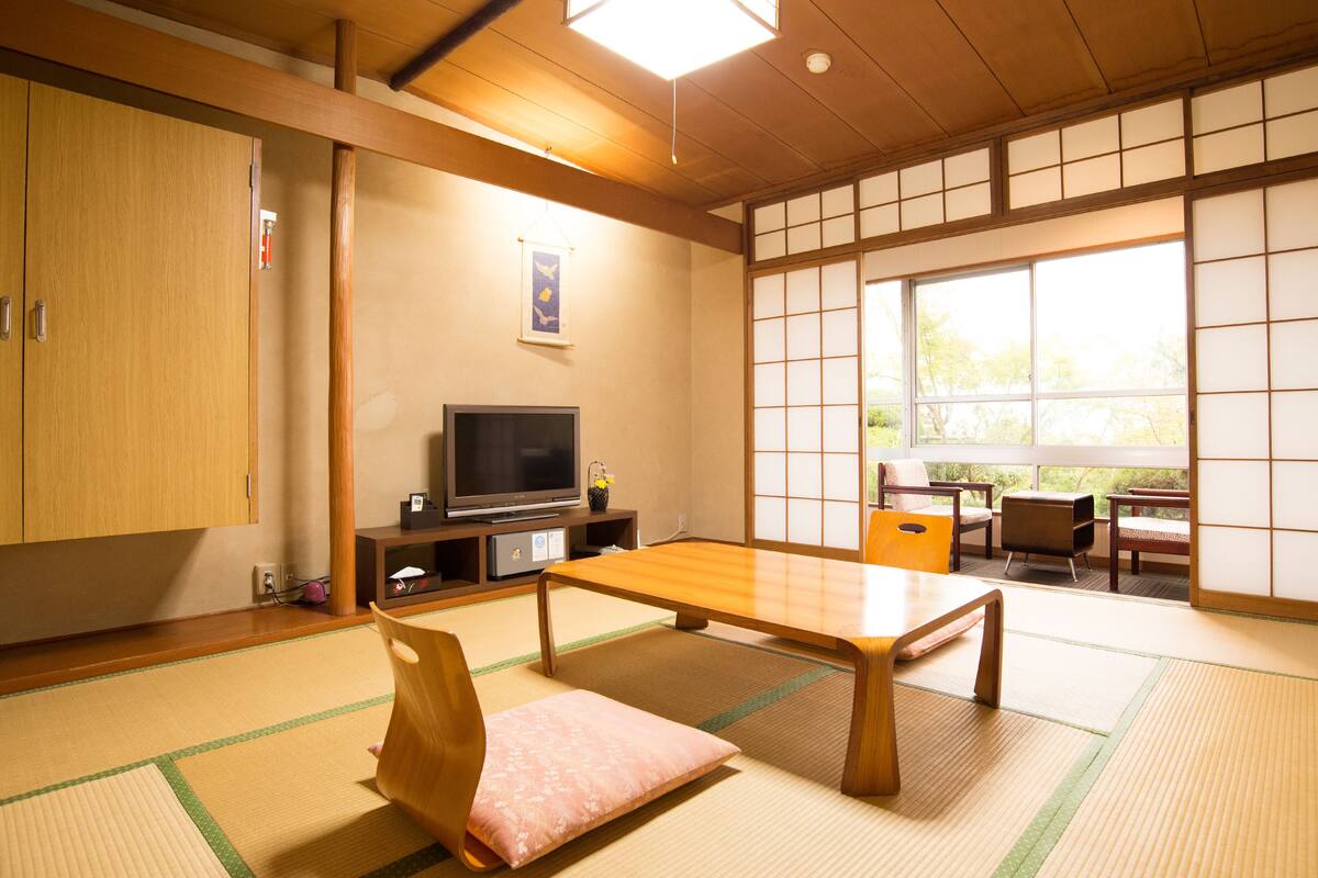 A traditional Japanese room with tatami flooring, a low table, a television, and sliding doors.