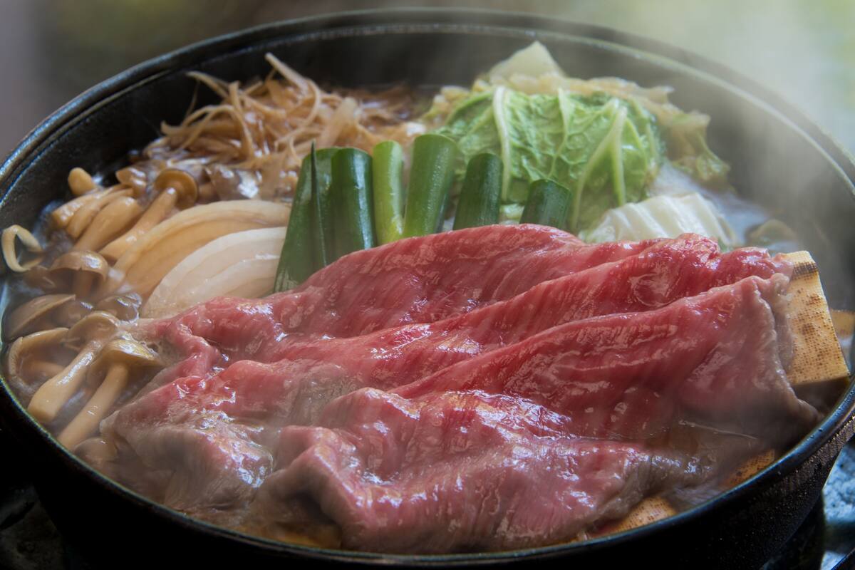 A hot pot with various ingredients including meat, vegetables, and mushrooms.