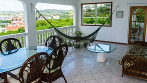 A room with a glass table, wicker chairs, a hammock, and a view of a town. - Cleopatra Villas (Gros Islet)