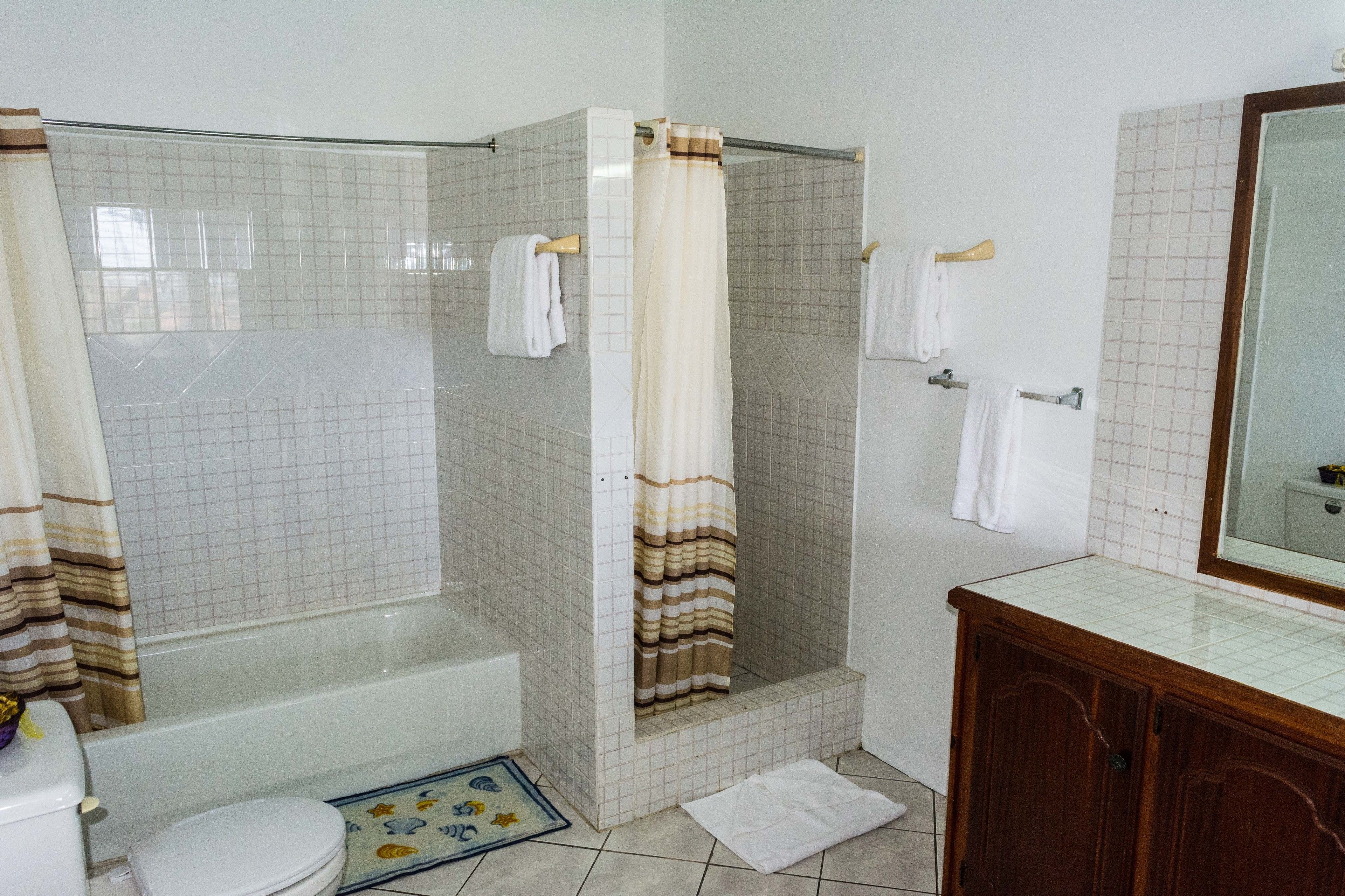 A bathroom with a bathtub, shower, toilet, and a wooden cabinet.