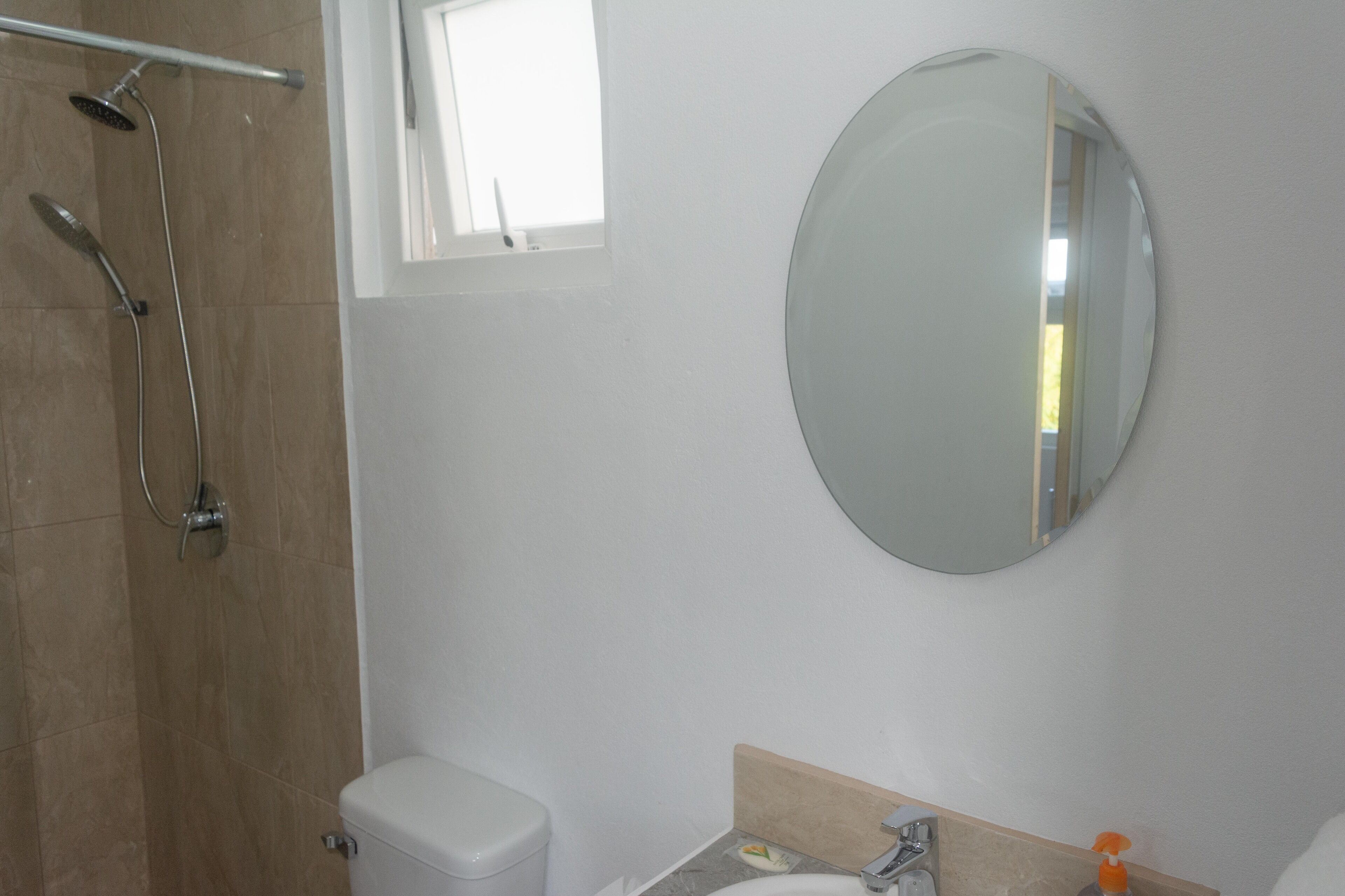 Un baño con inodoro, lavabo, espejo y ducha.