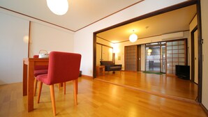A spacious room with wooden flooring, a red chair, a small table, and a sliding door leading to another area with a sofa and a TV.