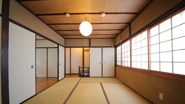 A traditional Japanese room with tatami flooring, sliding doors, and a large window with paper shades.
