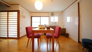 A dining area with a wooden table and four chairs, a kitchen in the background, and a sliding door on the left.