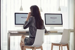 Une femme est assise à un bureau devant deux écrans d’ordinateur qui affichent le logo de la chaîne « Mercure Hotels ».