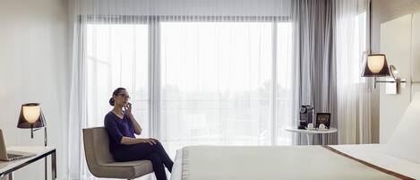 A hotel room with a large bed, a desk with a laptop, a chair, a coffee maker, and a small table with a picture frame.
