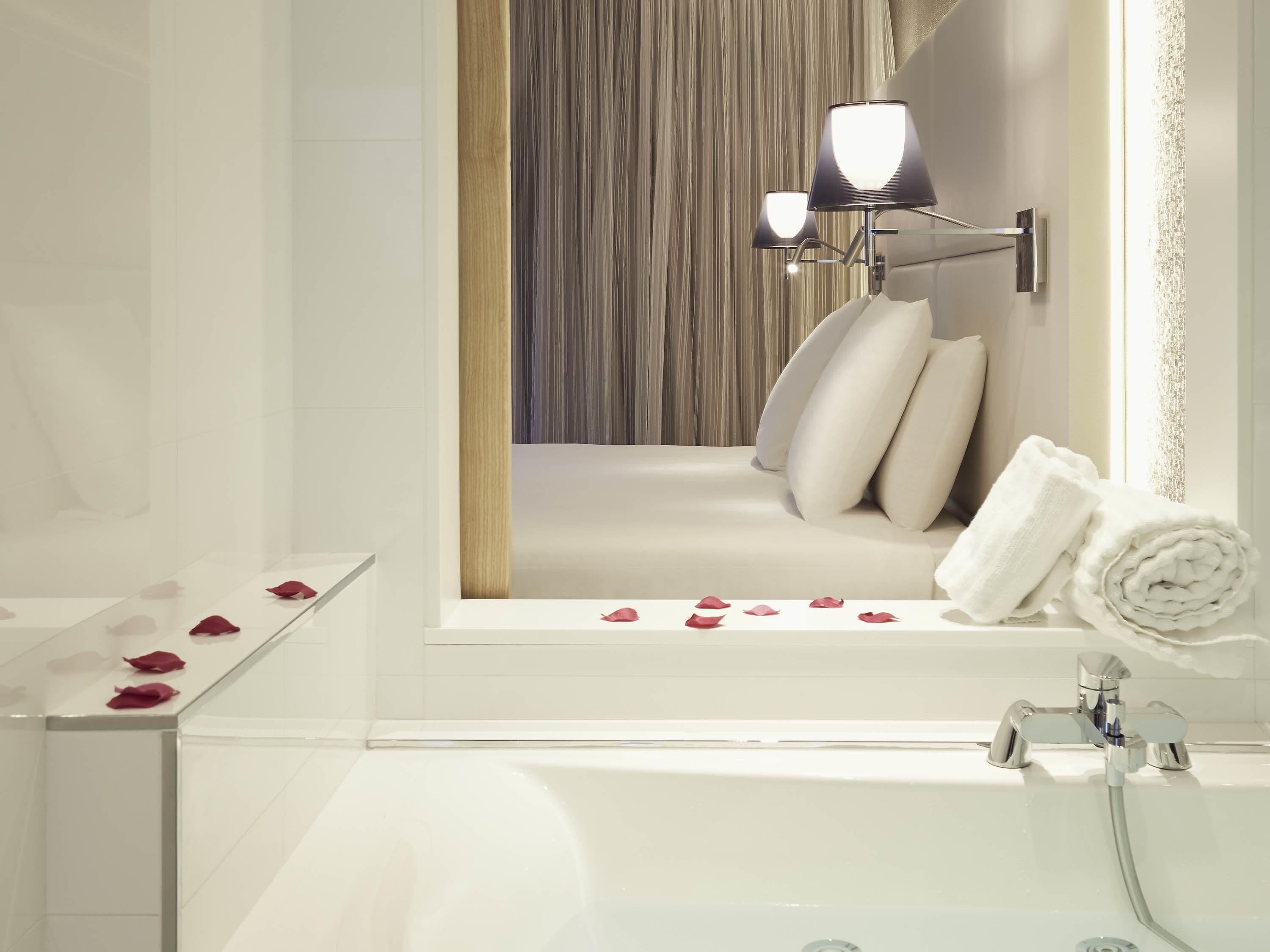 Une salle de bain moderne avec une baignoire, un miroir et un luminaire fixé au mur.