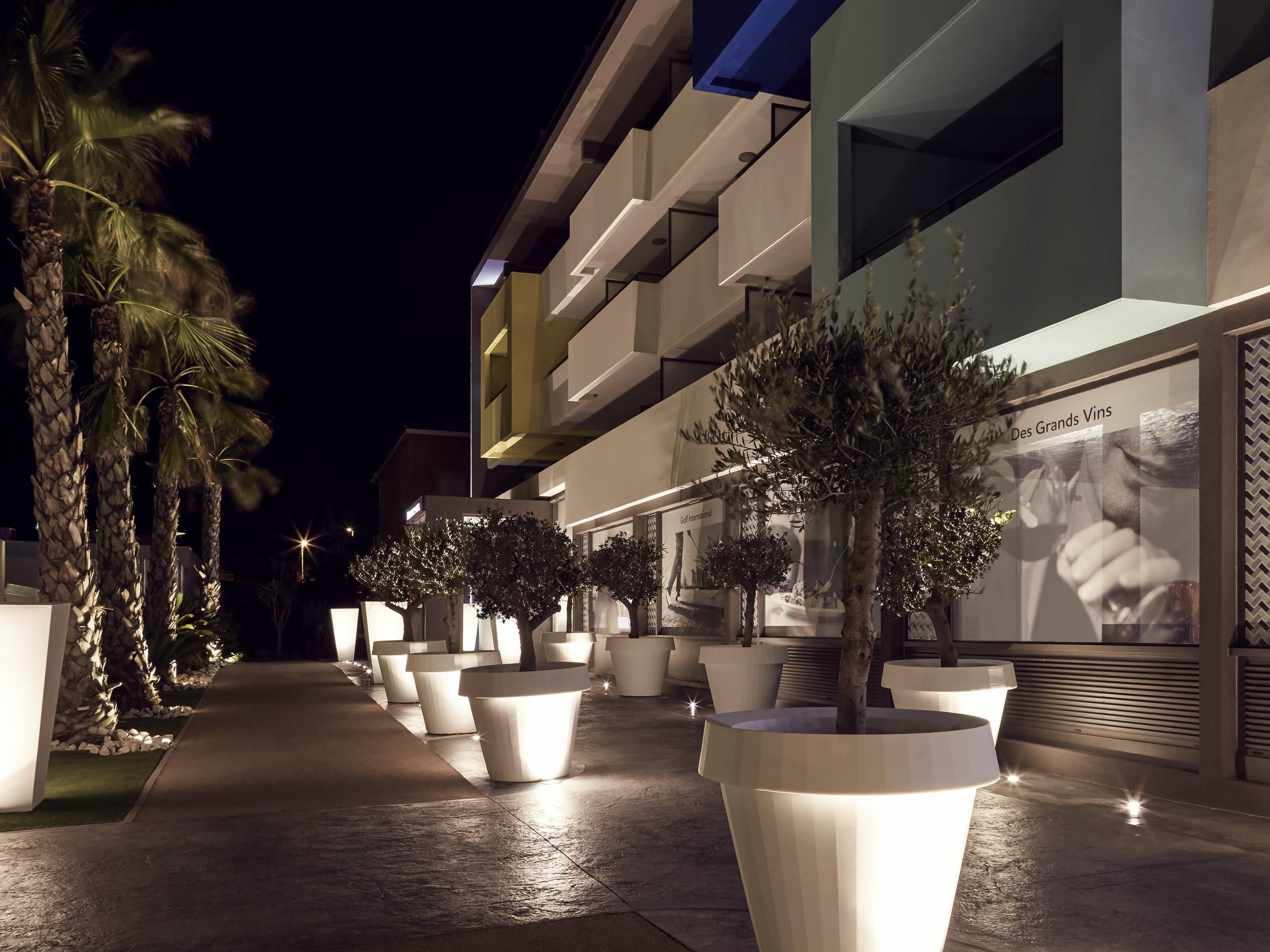 A modern building with a well-lit outdoor area featuring large planters and palm trees.