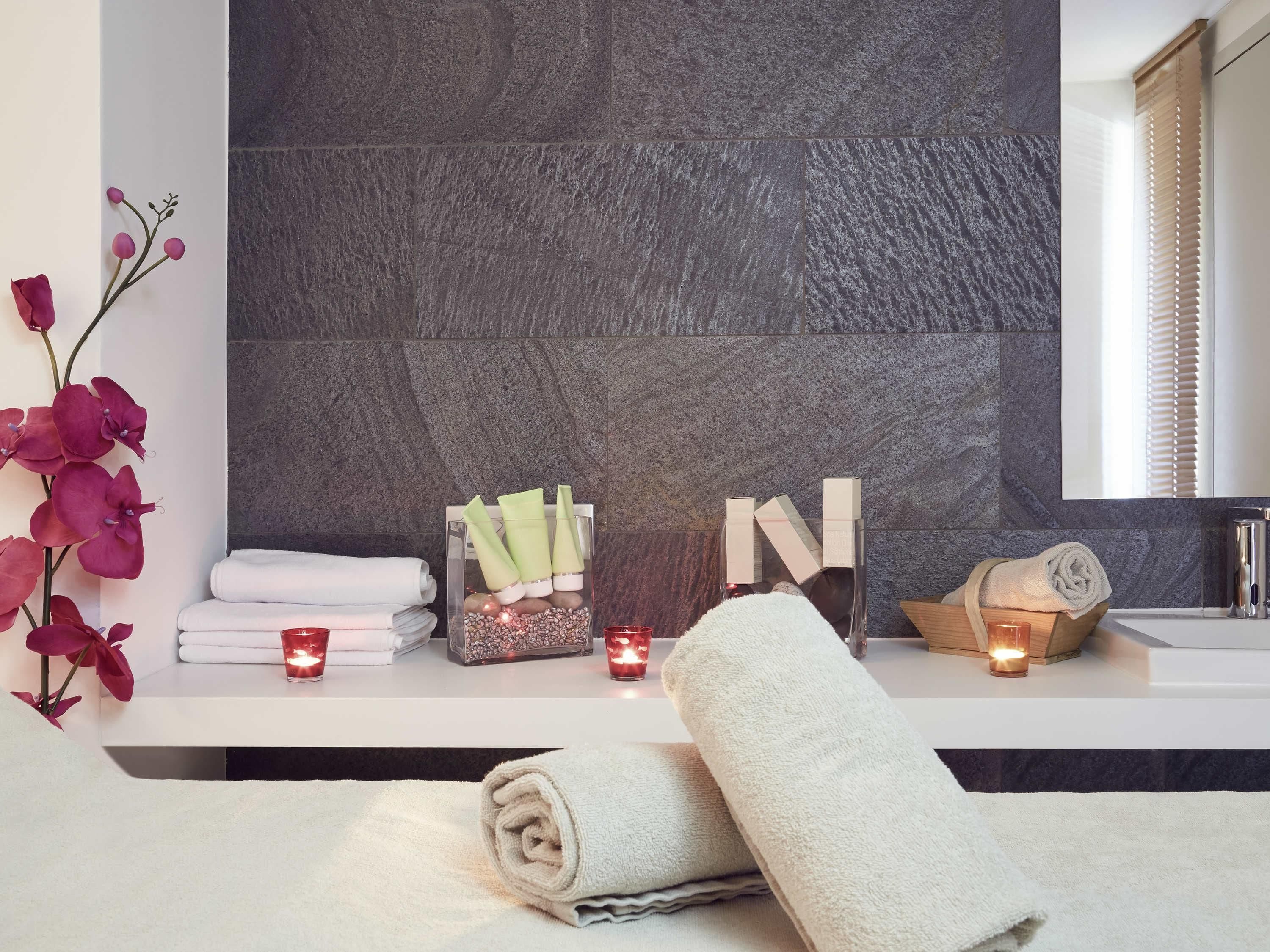 Een badkamer met een stenen muur, een spiegel, handdoeken, kaarsen en een decoratieve orchidee.