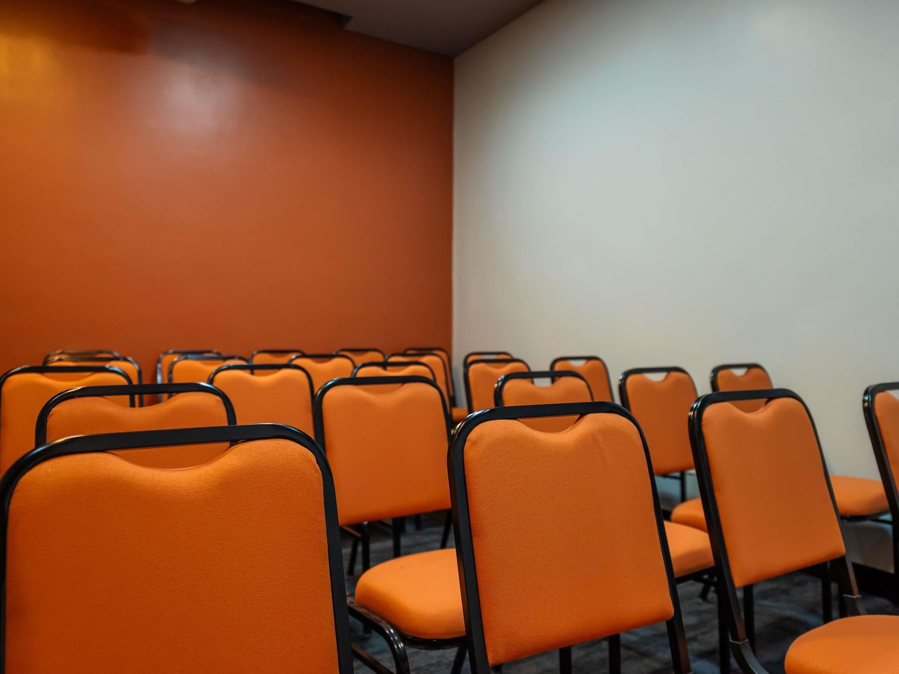 Un salón de conferencias con hileras de sillas anaranjadas y una pared lisa.