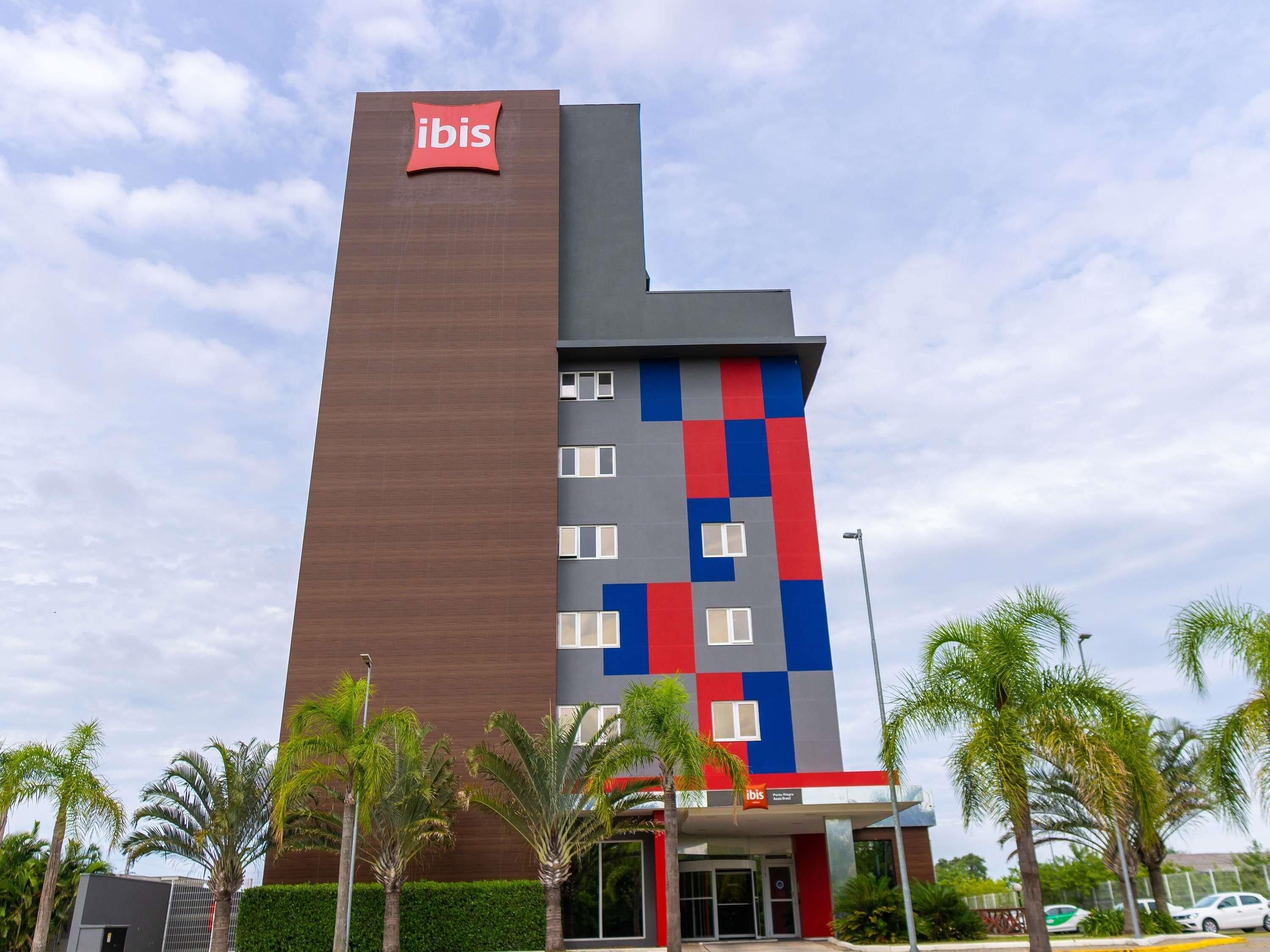 Ein Hotel mit gut sichtbarem Ibis-Logo, modernem Design und einer Farbgebung aus Rot, Blau und Grau, sowie einem Flachdach.