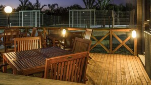 An outdoor wooden deck with tables and chairs, surrounded by a metal fence and palm trees. - ibis Porto Alegre Assis Brasil (Porto Alegre)