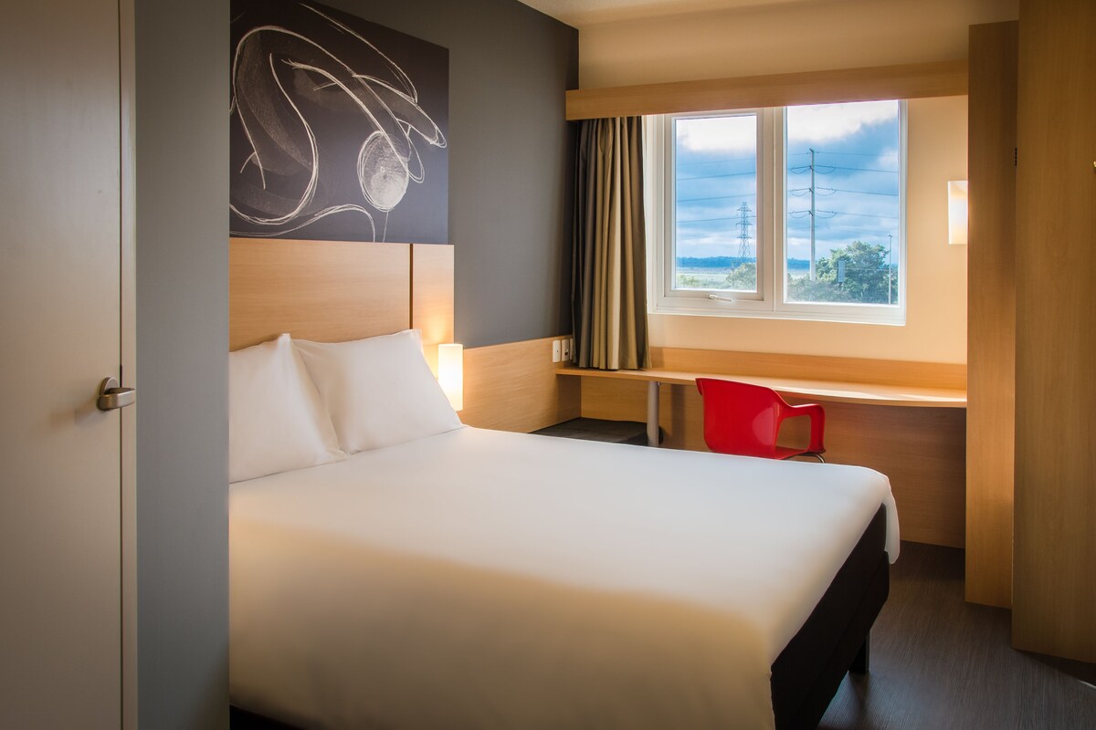 A hotel room with a bed, a desk, a chair, and a window with a view.