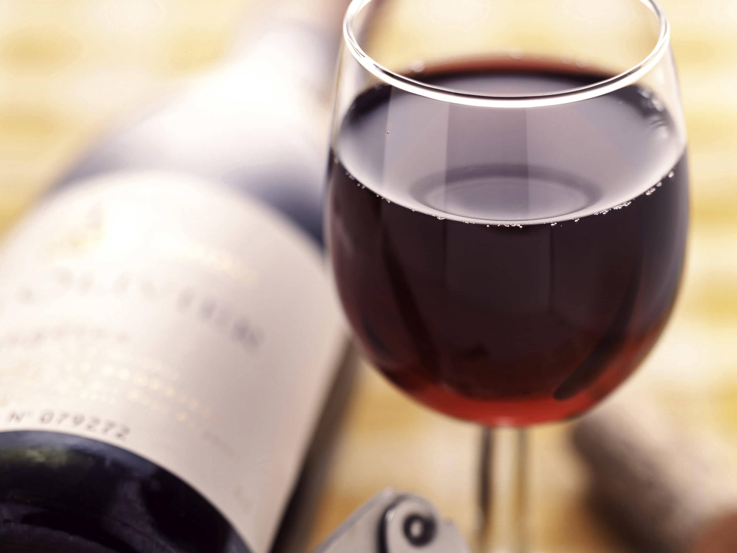 Una copa de vino tinto llena junto a una botella de vino abierta.