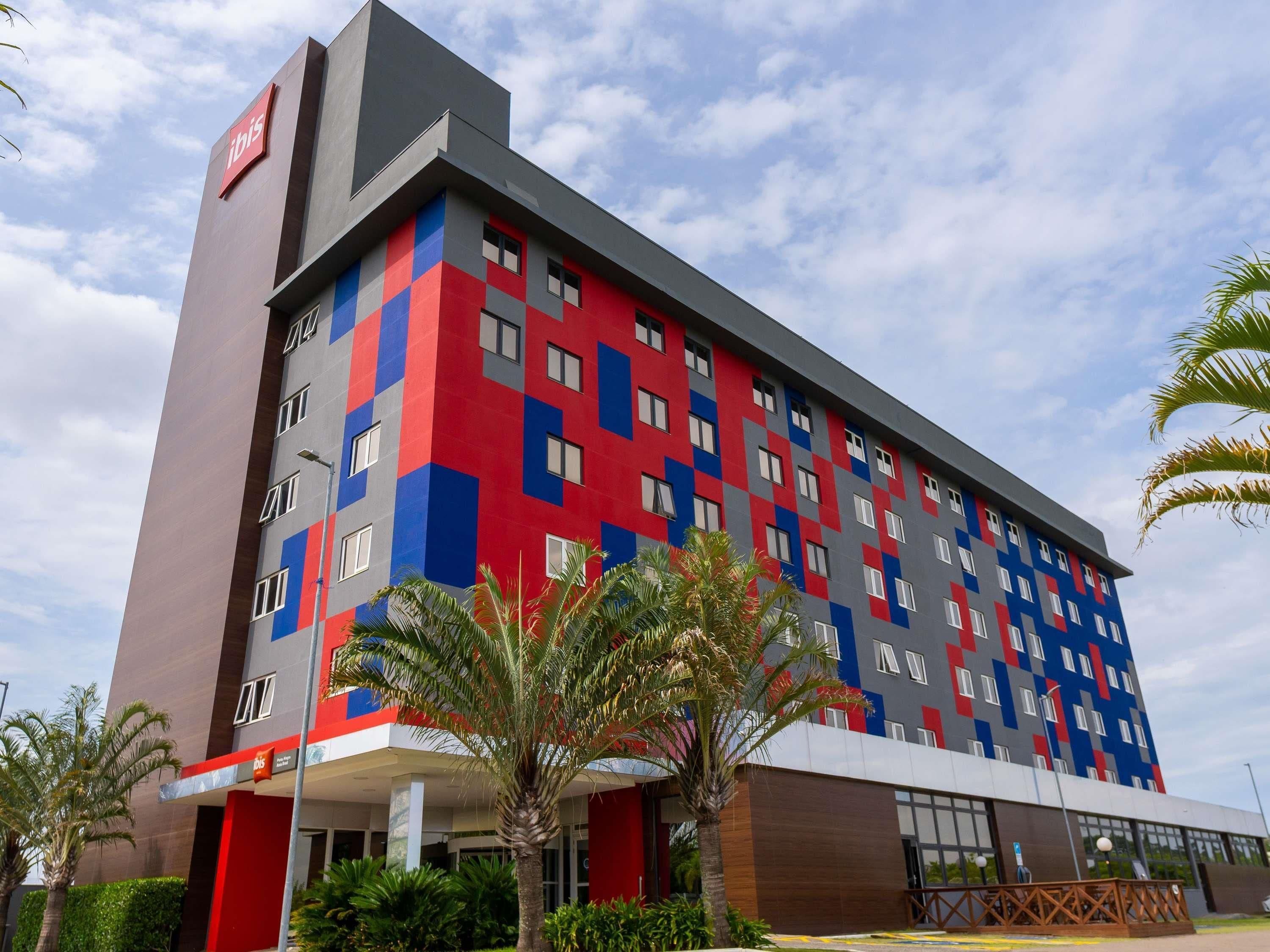 Um hotel com várias andares e fachada moderna, combinando cores vermelho, azul e cinza.